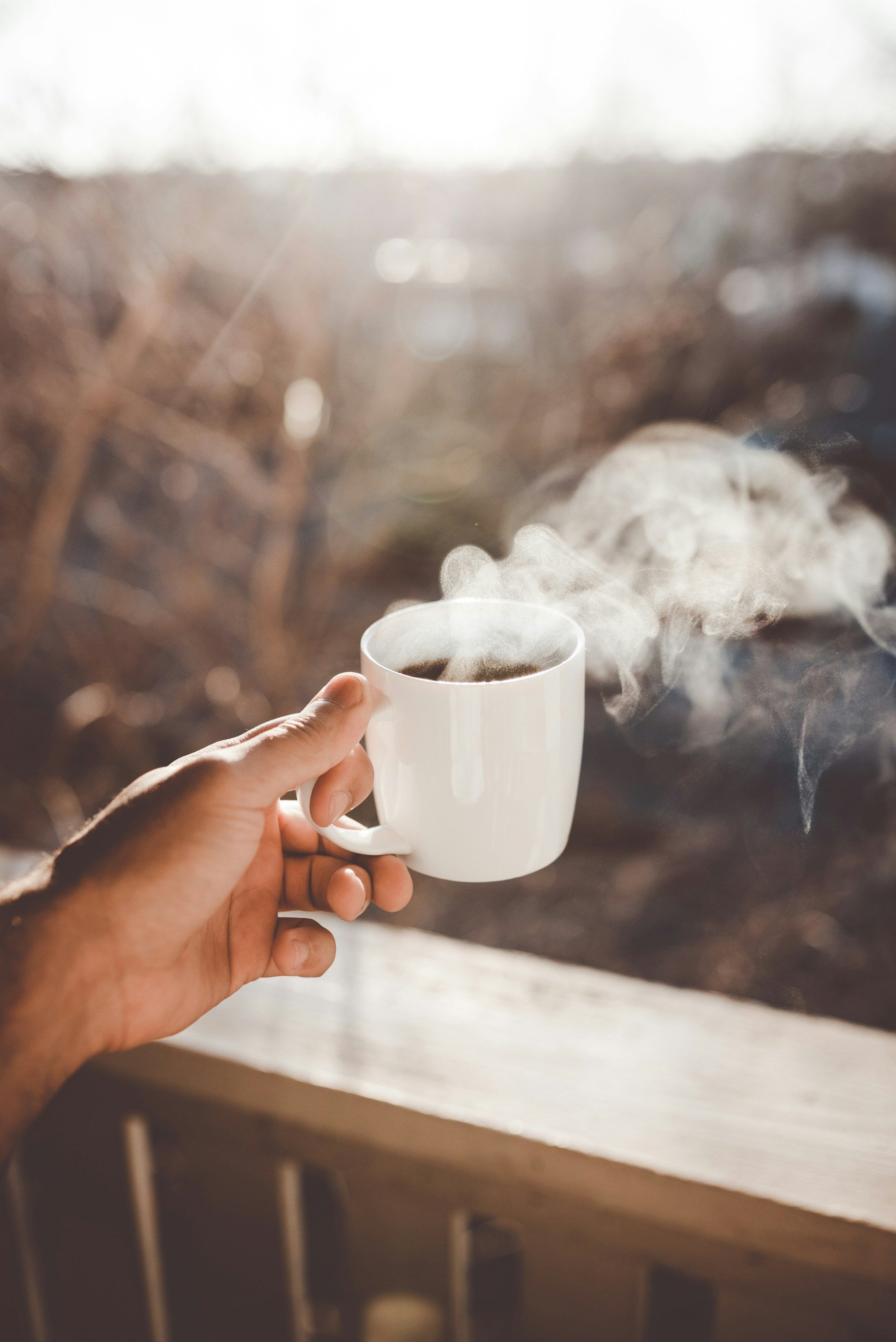 A hand holding a steaming mug of coffee against a blurred winter landscape