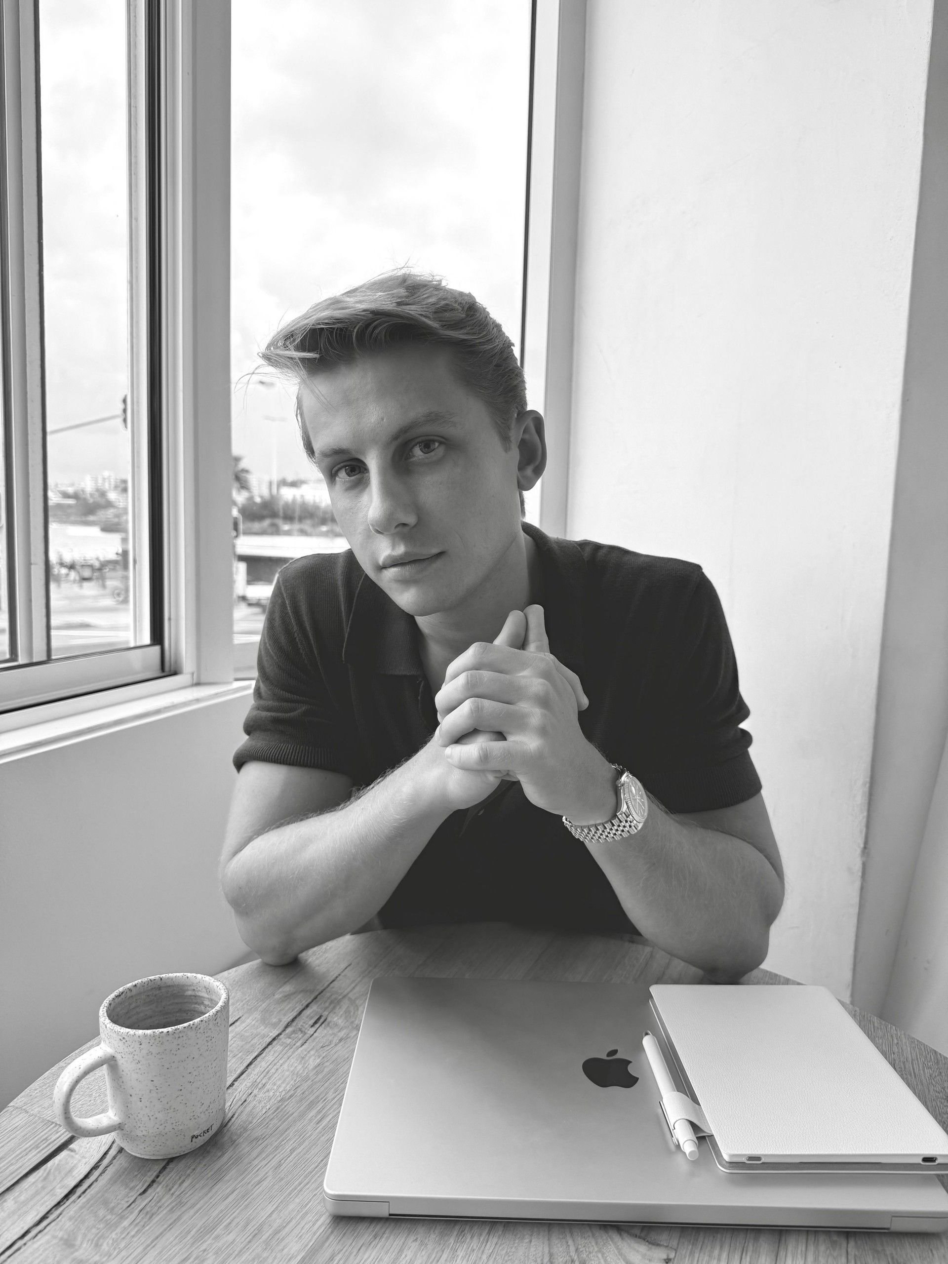 Adam Love sitting at a cafe table with a laptop and coffee, black and white